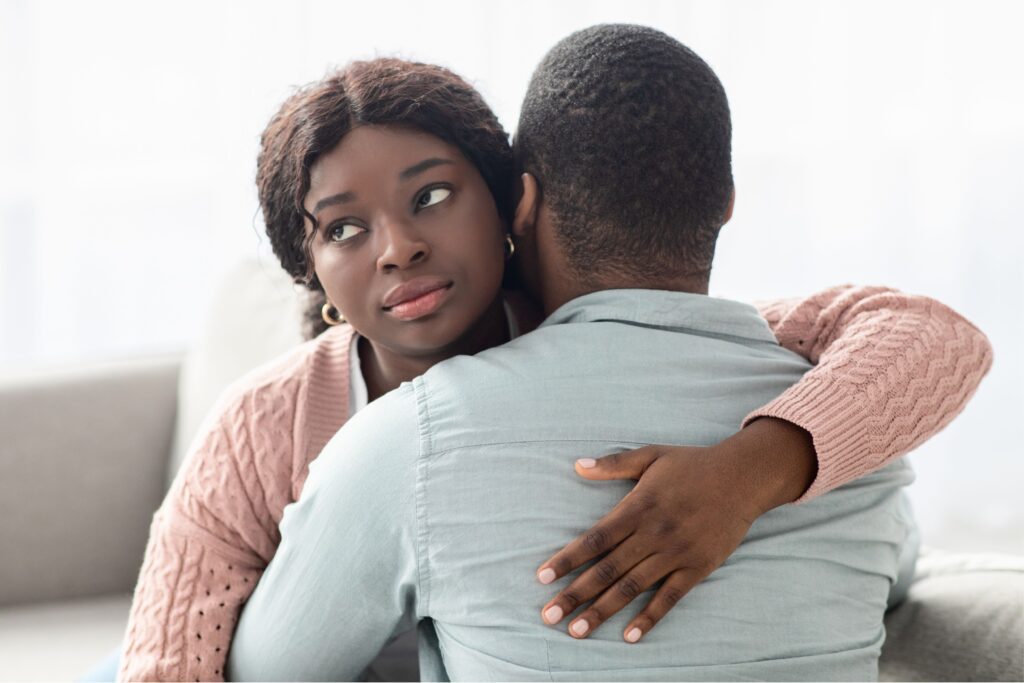 black woman looking away over the shoulder of the black man she's hugging indifferently