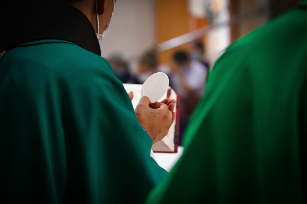 offering of gift of bread at holy mass during ordinary time, priests wearing green vestments, green chasuble